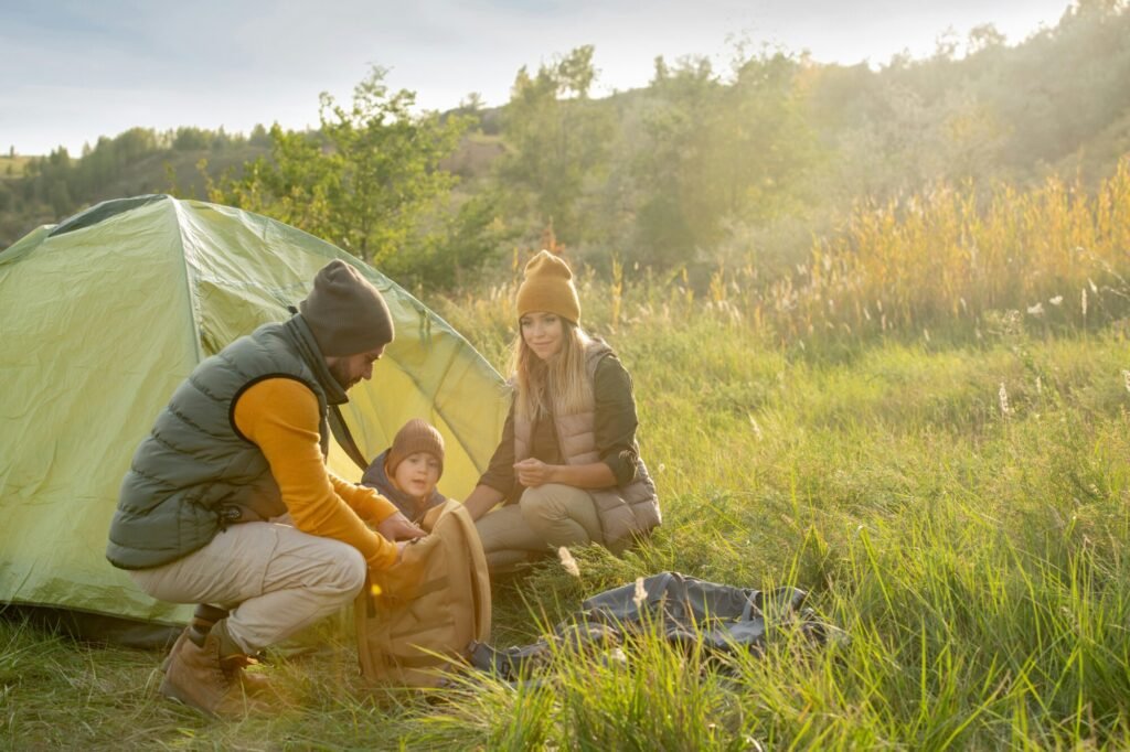 Mother, father, and son crouch next to their tent in a meadow, camping with kids.